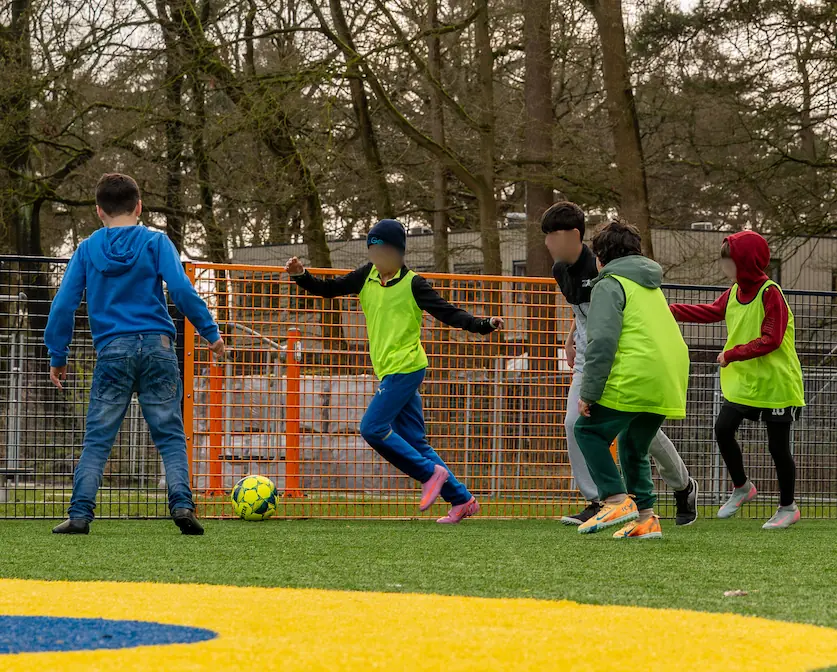 AZC kinderen van gemixte afkomsten die samen aan het voetballen zijn. Ze krijgen gelijke kansen tijdens de training.